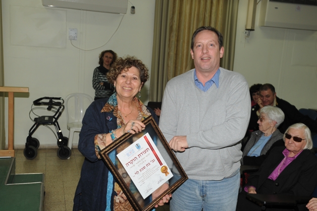 Yael Arbeli, the district nurse supervisor, offering a recognition certificate to the son of the first superintendent nurse, Mrs. Batsheva Levy 